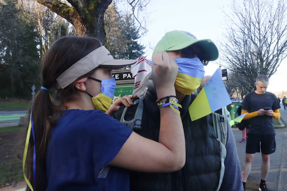 caption: Peyton Thomas paints Wendy Thomas' face. Both are wearing blue and yellow masks — the colors of the Ukrainian flag.