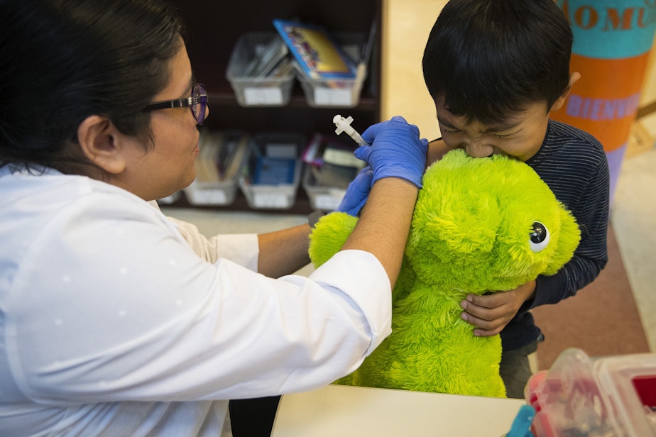 caption: Erika Sandoval, a nurse with the Seattle Visiting Nurse Association, gives kindergartener Javier Garcia Campos a flu shot on Tuesday, October 22, 2019, at Concord International Elementary School in Seattle.