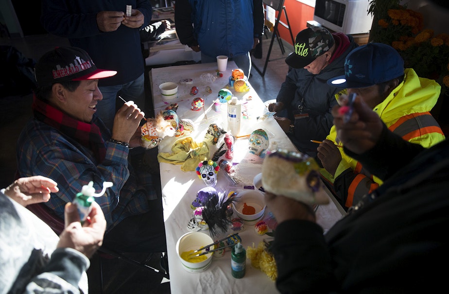 caption: Humberto Ramos, left, smiles while painting a calavera in preparation for the Day of the Dead altar on Tuesday, October 29, 2019, at Casa Latina in Seattle.