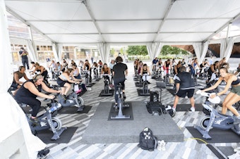 caption: People attend a SoulCycle class under an outdoor tent in September in New York City.