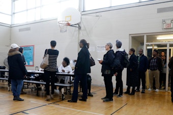 caption: People stand in line at a Detroit polling place during Michigan's March 10 presidential primary. As a result of the pandemic, the state's top election official is sending absentee ballot applications to every registered voter for August and November elections.