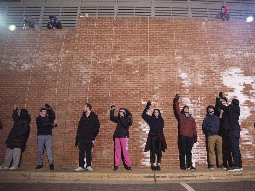 caption: <em></em><em>Survivor Maryland</em> crewmembers tie participants' arms to cups of water before the challenge begins. After it starts, some players start singing Journey's "Don't Stop Believin'" to distract from the cold.