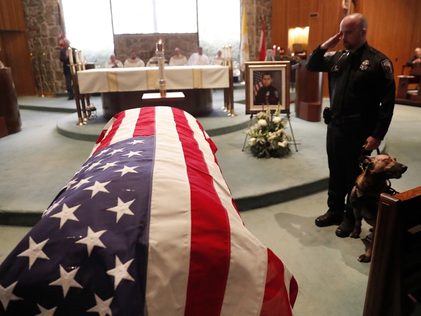 caption: As of Dec. 27, this year 144 federal, state and local law enforcement officers have died in the line of duty — a rise from the 129 officers killed in 2017. Here, wounded Dekalb County Police K9 Indi stands by his handler's side during a funeral service for Edgar Flores on Dec. 18 in Georgia.