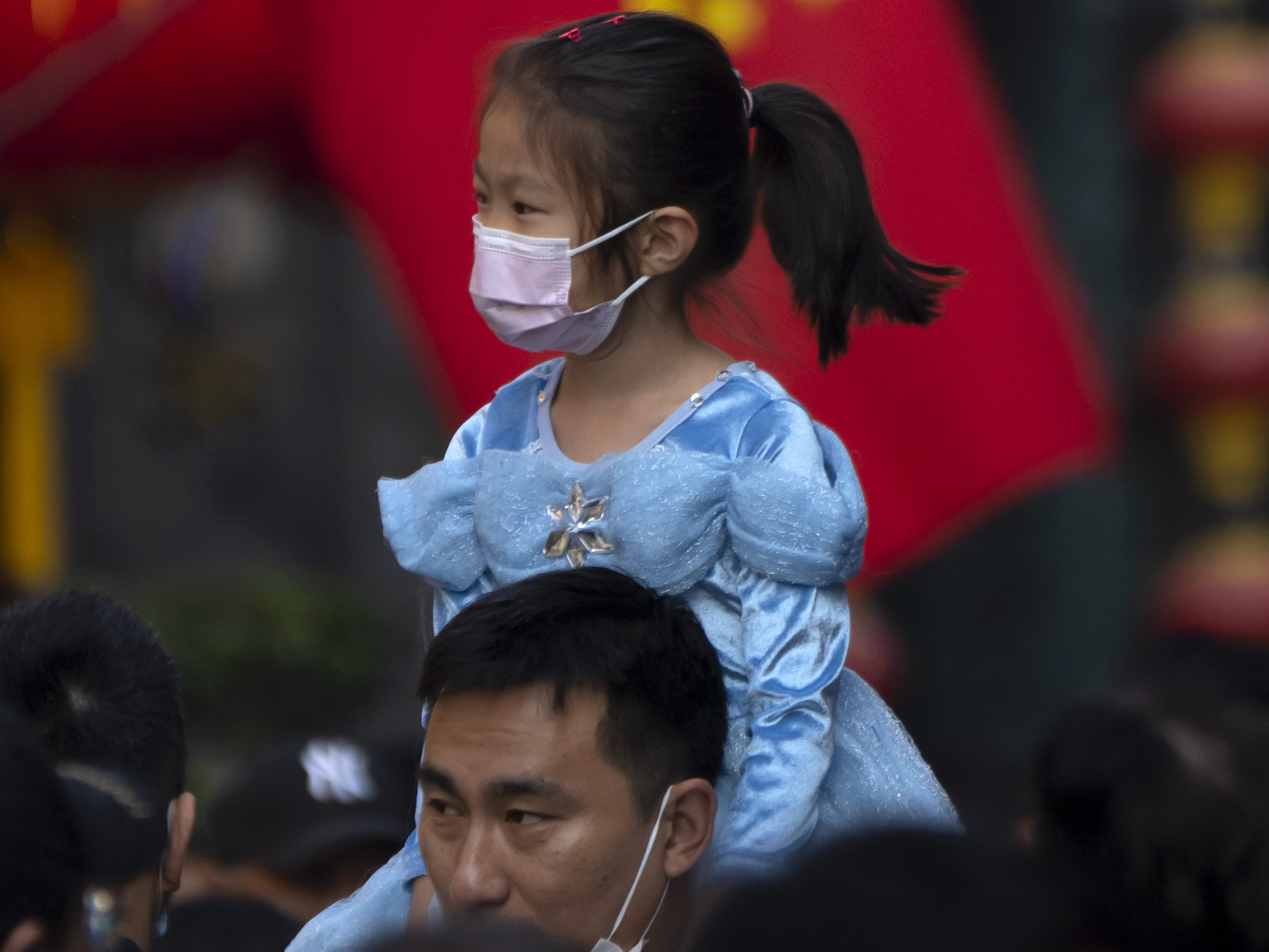 caption: A girl rides on a man's shoulders as they walk along a shopping street in Beijing. China has announced its first overall population decline in recent years amid an aging society and plunging birthrate.