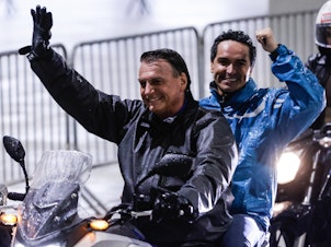 caption: President Bolsonaro rides a motorbike with a supporter during a campaign rally in Santos on Wednesday.