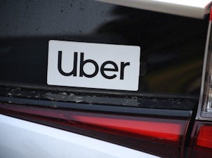 caption: An Uber sticker is seen on a car at the start of a protest by ride share drivers on Aug. 20, in Los Angeles. Uber said it will sell its self-driving research unit to startup Aurora.