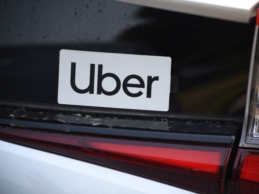 caption: An Uber sticker is seen on a car at the start of a protest by ride share drivers on Aug. 20, in Los Angeles. Uber said it will sell its self-driving research unit to startup Aurora.