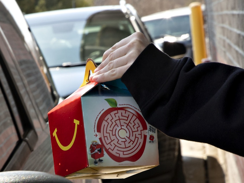 caption: McDonald's says it will phase out most plastic from its Happy Meals by 2025. Here, a customer picks up a kid's meal at a McDonald's drive-through.