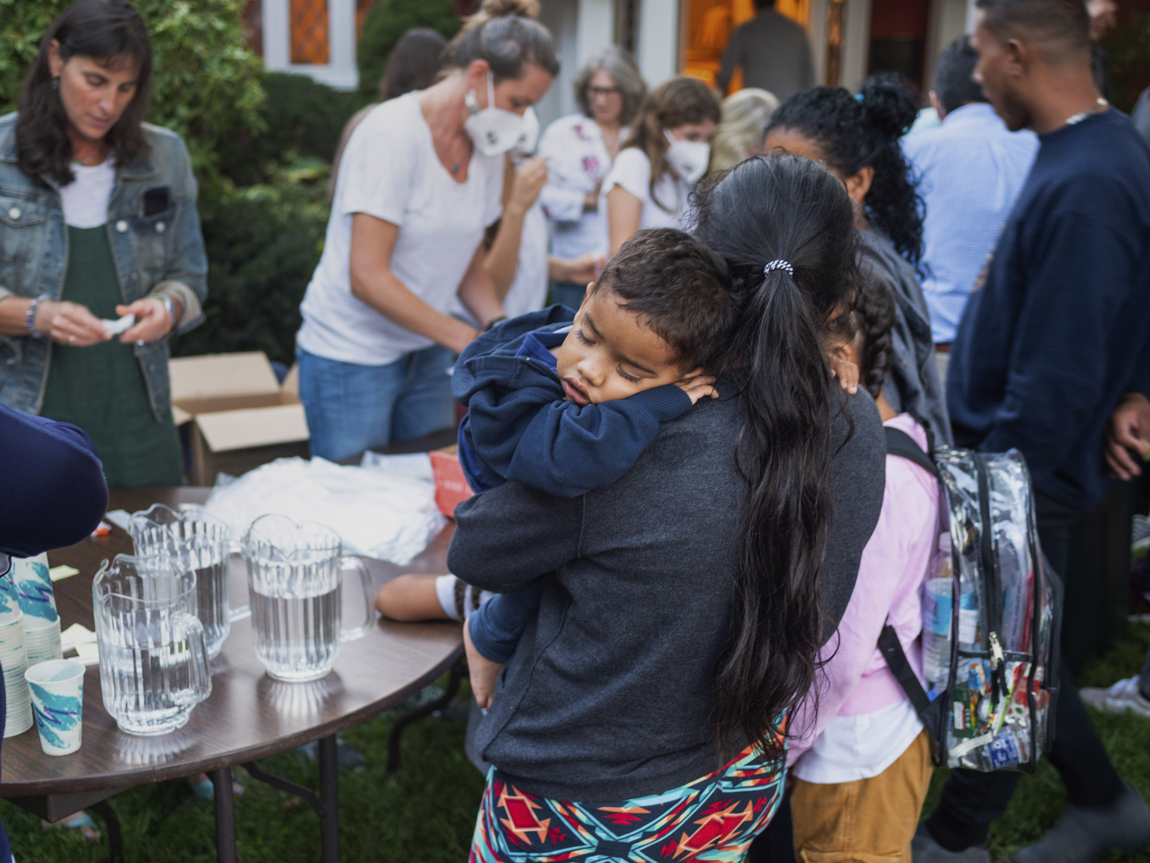 caption: A woman, who is part of a group of migrants that had just arrived, holds a child as they are fed outside St. Andrews Episcopal Church, Wednesday Sept. 14, 2022, in Edgartown, Mass., on Martha's Vineyard. Fla. Gov. Ron DeSantis flew two planes of migrants to Martha's Vineyard on Wednesday.