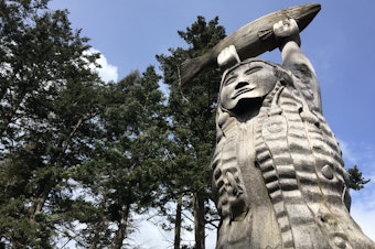 caption: A cedar carving of Ko-Kwal-Alwoot, the Maiden of Deception Pass, with hair turned to ribbons of kelp, holds a salmon aloft at Deception Pass State Park.