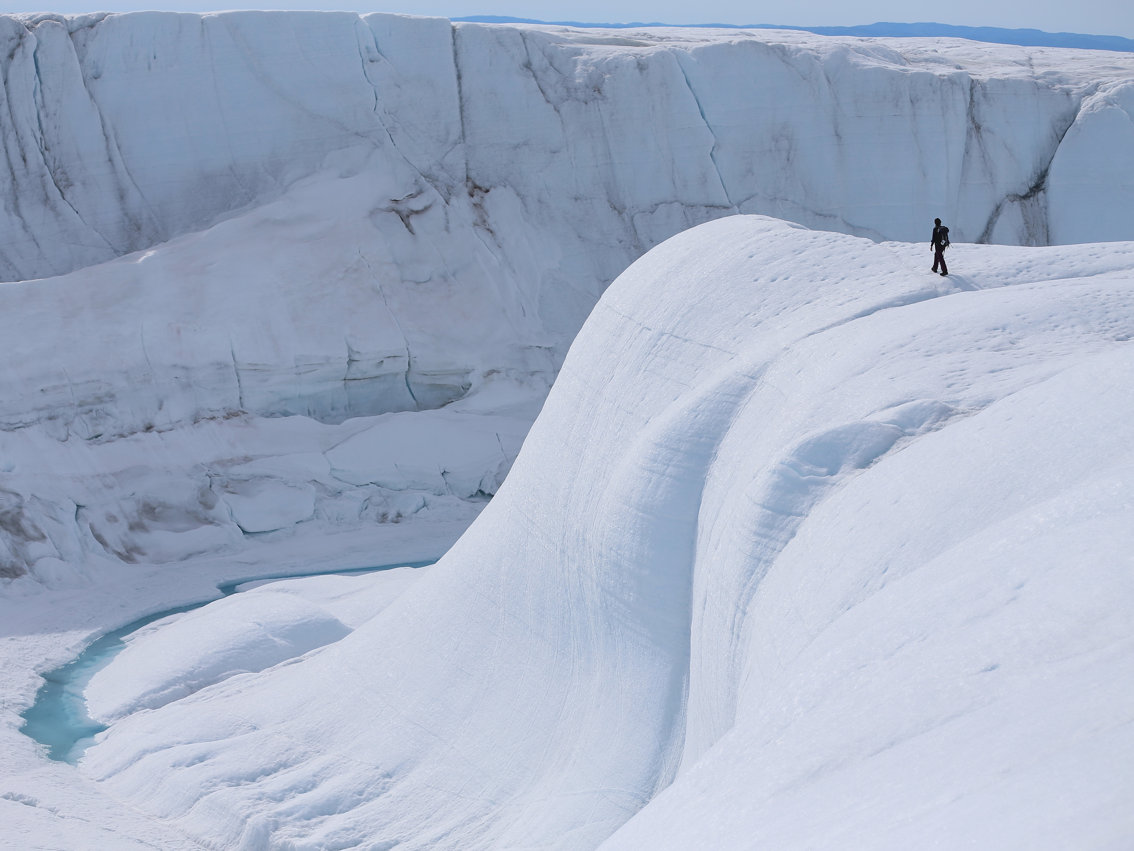caption: A researcher looks at a canyon created by a meltwater stream on the glacial ice sheet in Greenland in 2013.
