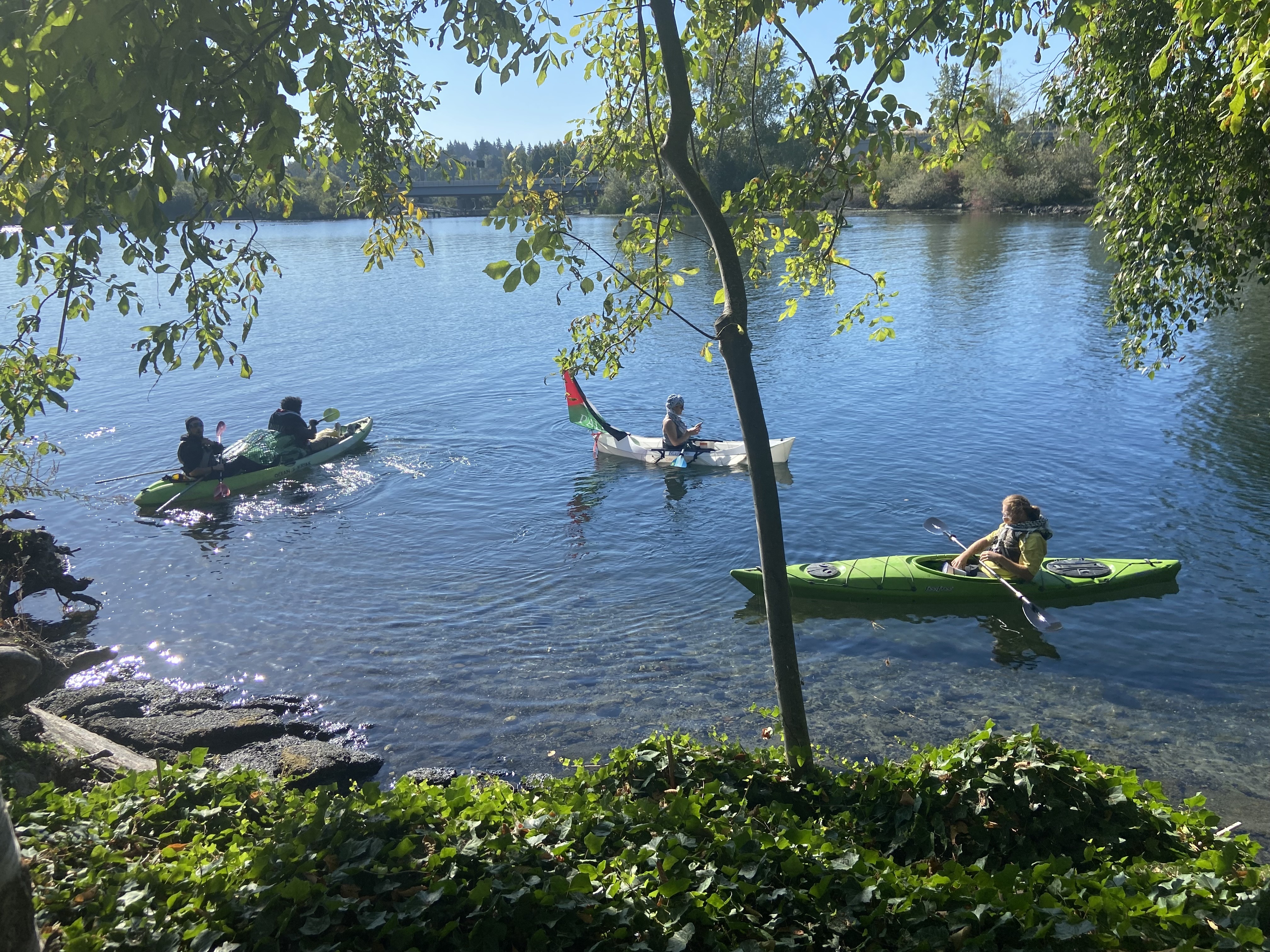 caption: Five protestors appeared via kayak outside of the University of Washington’s ground breaking ceremony for the ASUW Shell House. The protestors called on the university to divest from companies associated with Israel’s war in Gaza.