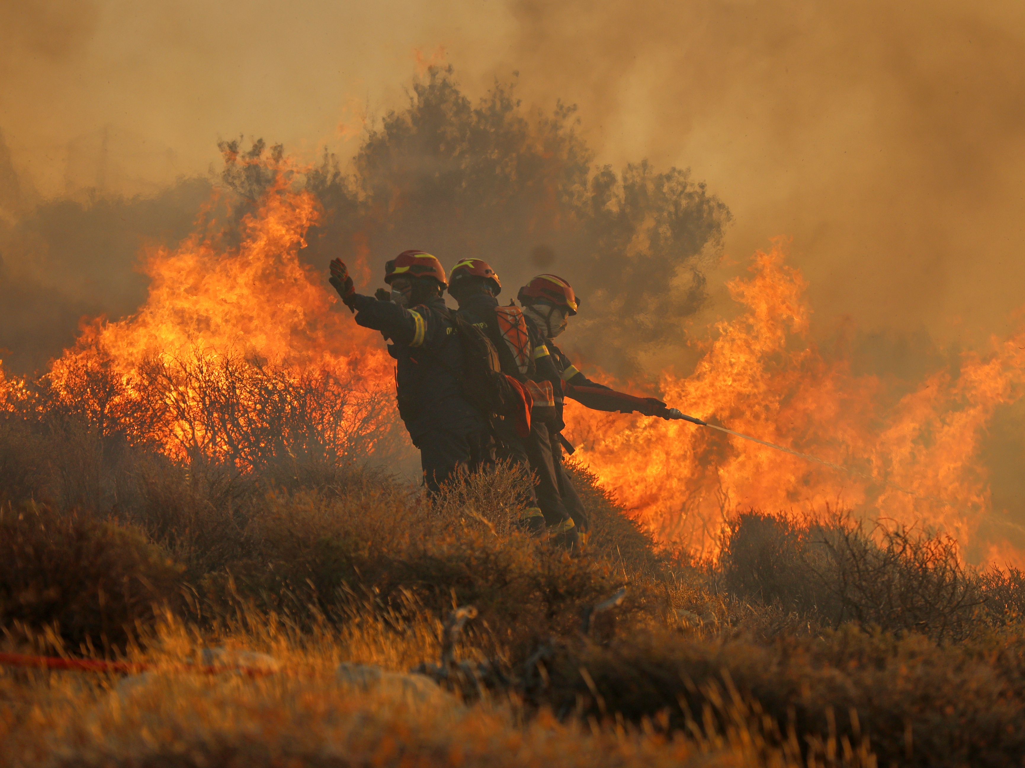 caption: Firefighter uses a hose as the try to extinguish the blaze near the town of Ierapetra on the south coast of Crete island, Greece on Thursday as a fast-moving wildfire prompted authorities to clear villages and coastal areas, officials said.
