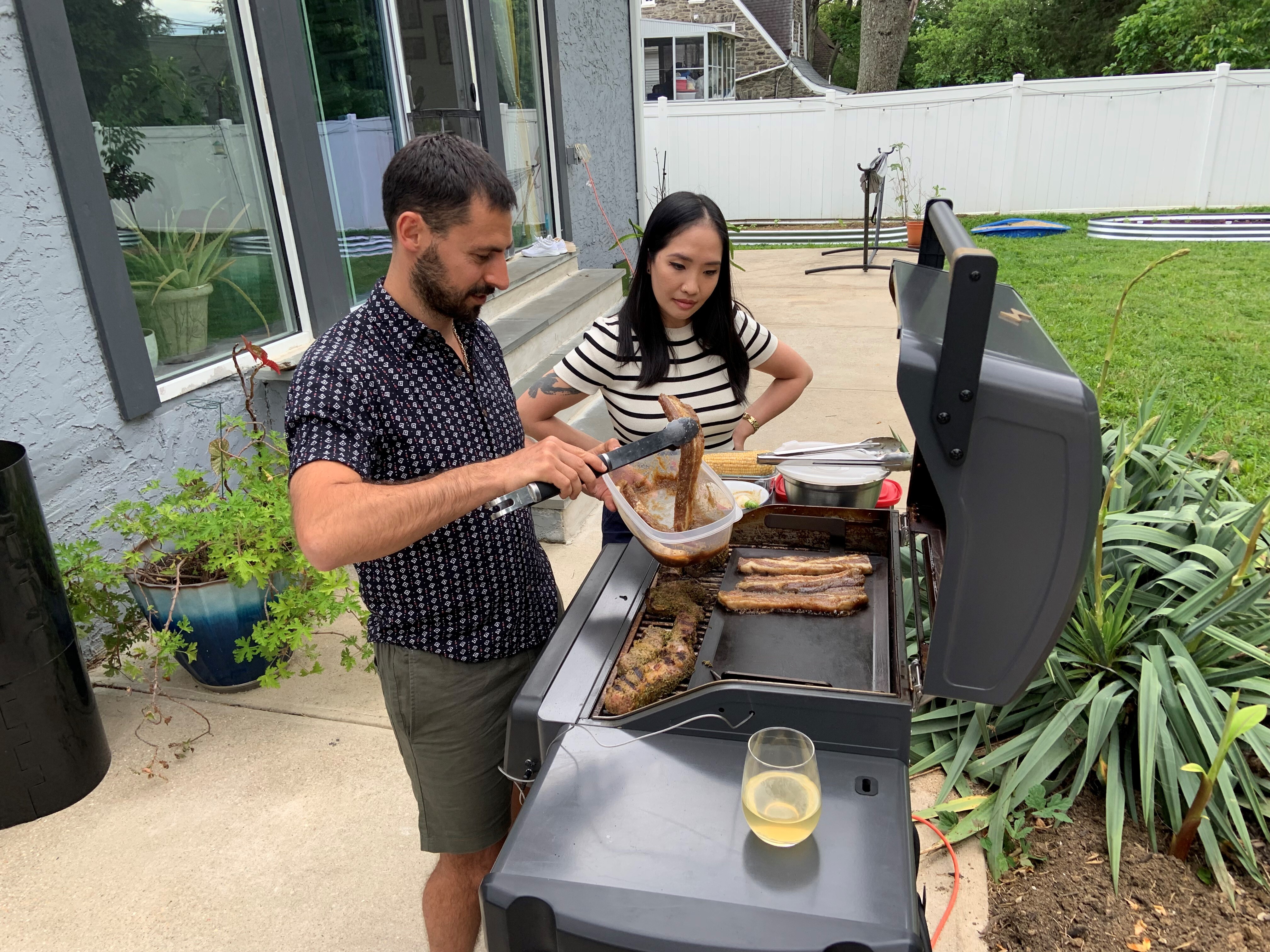 caption: Stoio Kachev and Doanh Nghiem cook dinner on their electric grill. The couple says convenience is the main reason they switched from a propane grill — no need to refill tanks. Switching to electric also reduces their contribution to climate change.