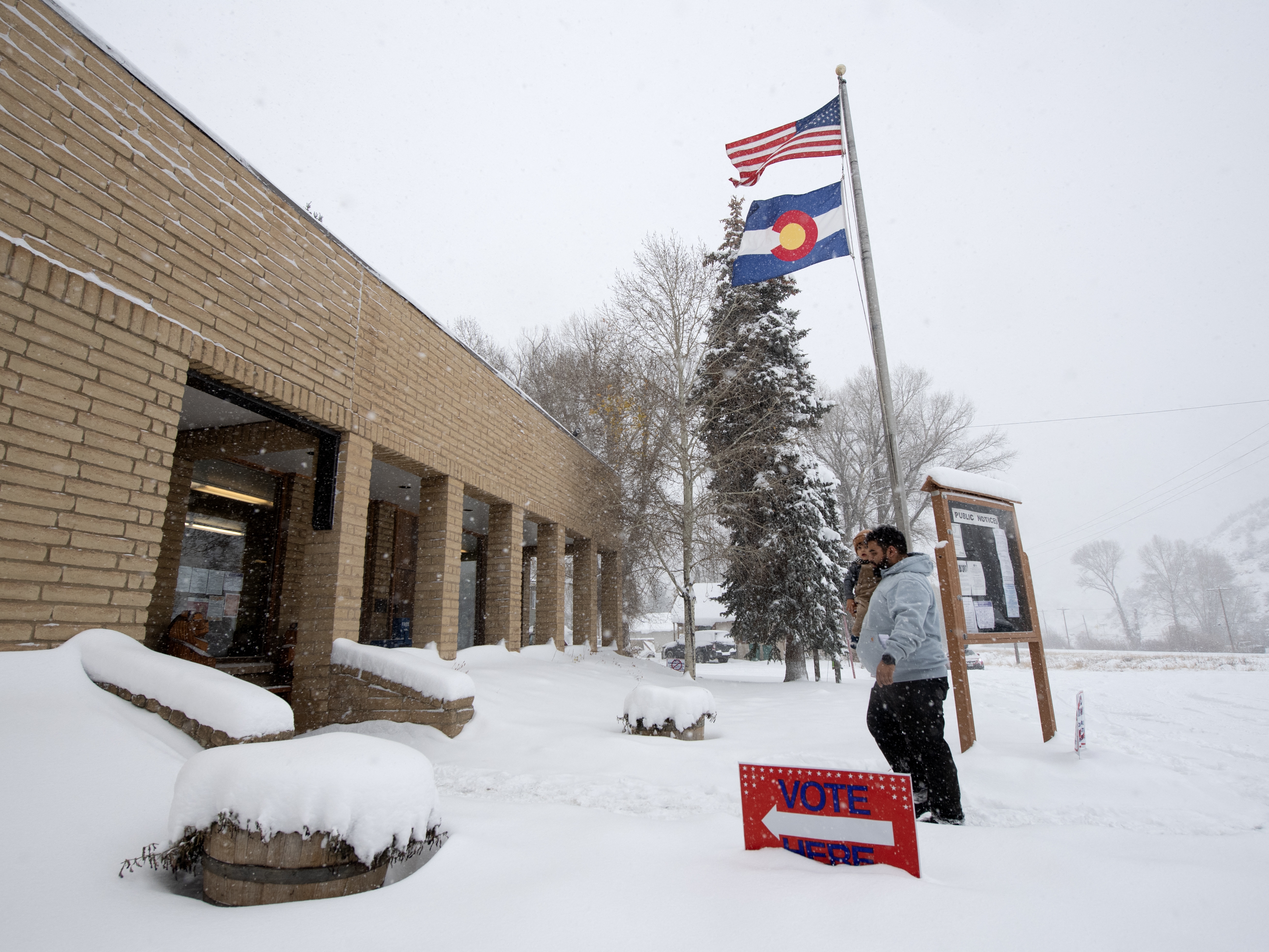 caption: A voter carries his son as he walks into the Oak Creek Town Hall to drop off his ballot on Election Day, Nov. 5, 2024, in Oak Creek, Colo.