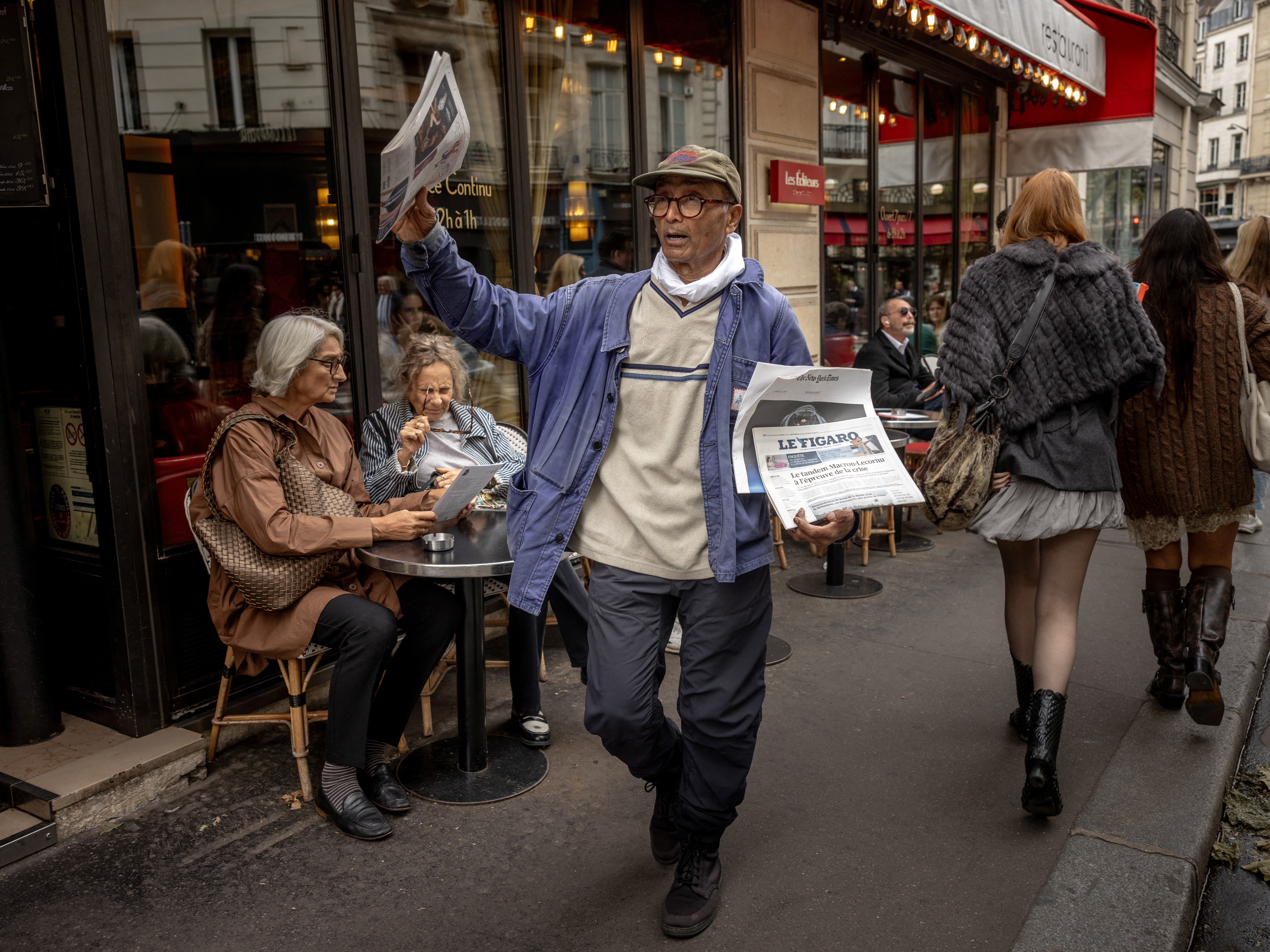 caption: Ali Akbar sells newspapers in the Latin Quarter in Paris in September 2025. The Pakistani-born 73-year-old is believed to be the last remaining newspaper vendor in the French capital, and was awarded a knighthood by France's President Emmanuel Macron last month.