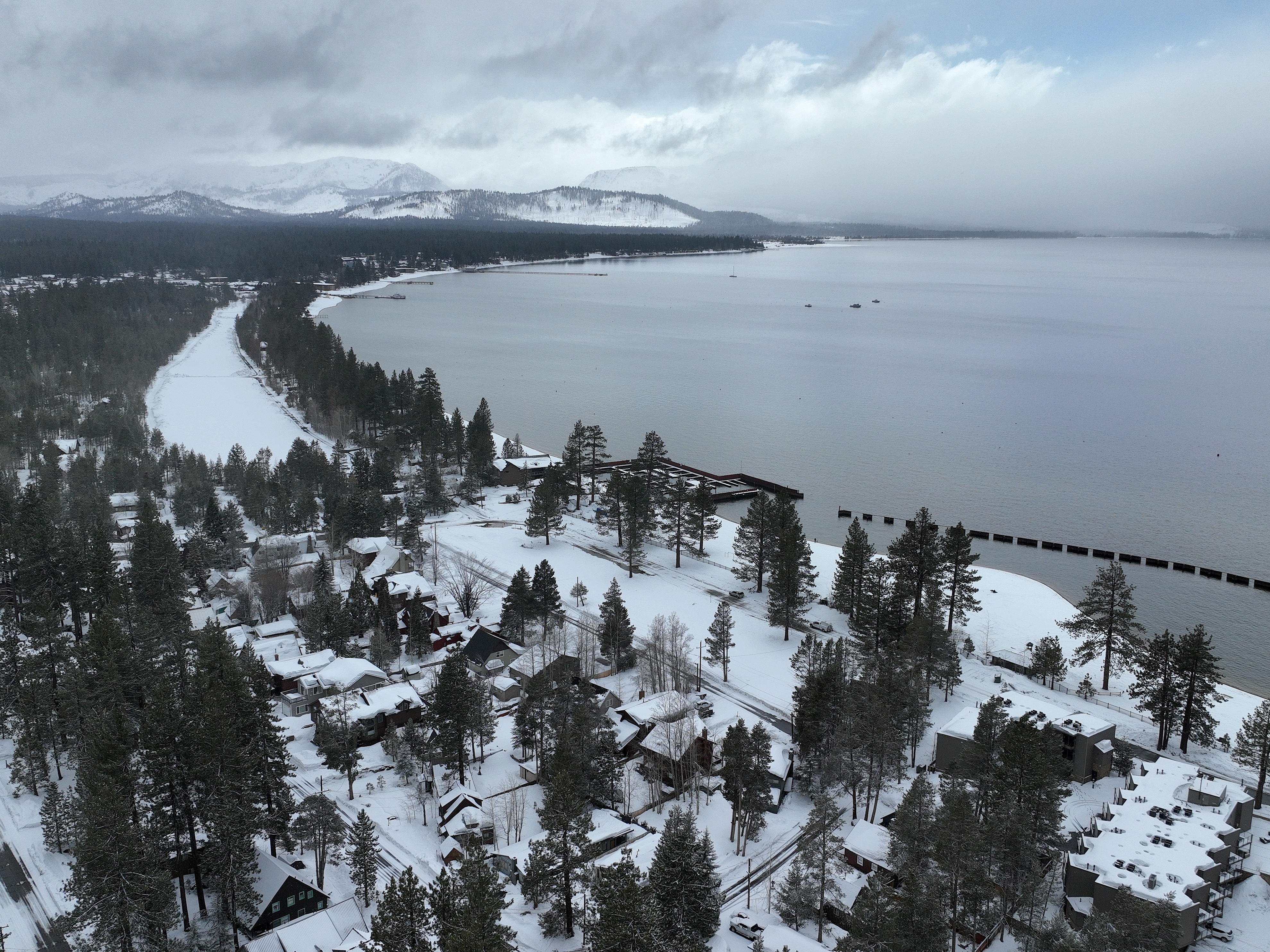 caption: In an aerial view, snow covers the banks of Lake Tahoe on March 21, 2023 in South Lake Tahoe, California.