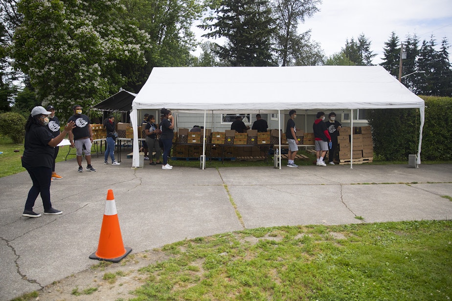 caption: Boxes of fresh produce, meat and dairy are stored under a tent before they are loaded into vehicles at a drive-thru free food distribution site led by the Pacific Islander Community Association of Washington on Thursday, July 10, 2020, along Military Road South in Kent. 