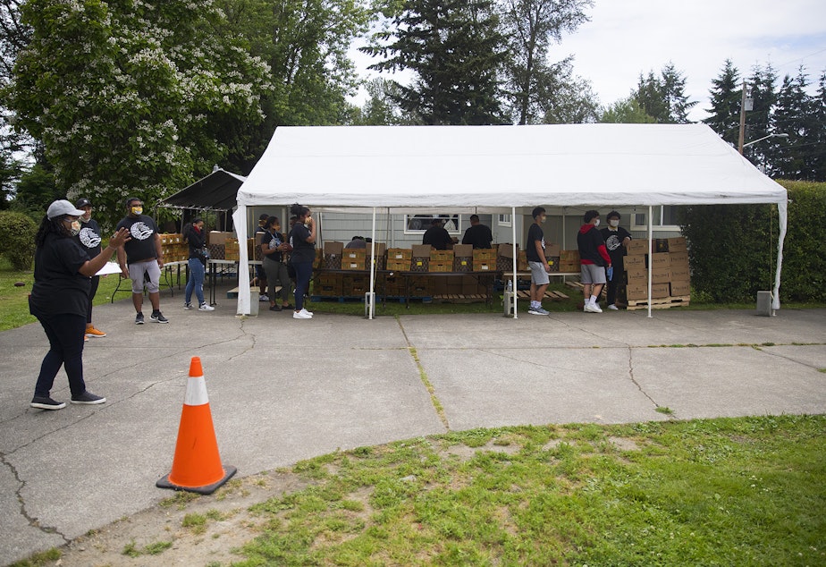 caption: Boxes of fresh produce, meat and dairy are stored under a tent before they are loaded into vehicles at a drive-thru free food distribution site led by the Pacific Islander Community Association of Washington on Thursday, July 10, 2020, along Military Road South in Kent. 