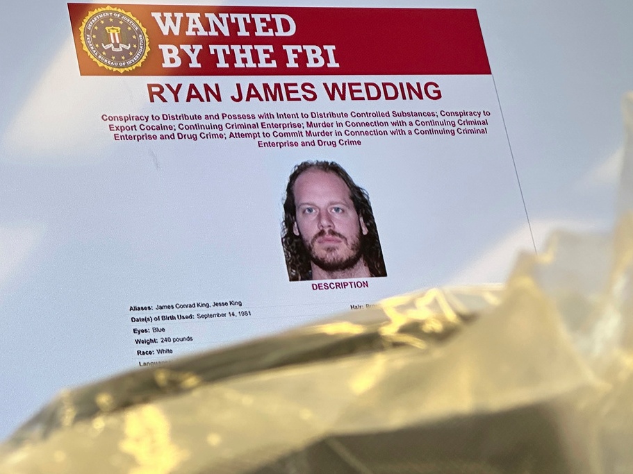 caption: An image of former Canadian Olympic snowboarder Ryan Wedding, who was a fugitive and had been charged with allegedly running and participating in a transnational drug trafficking operation, is displayed on a video monitor along with bricks of cocaine, foreground, during an October 2024 news conference at the FBI offices in Los Angeles.