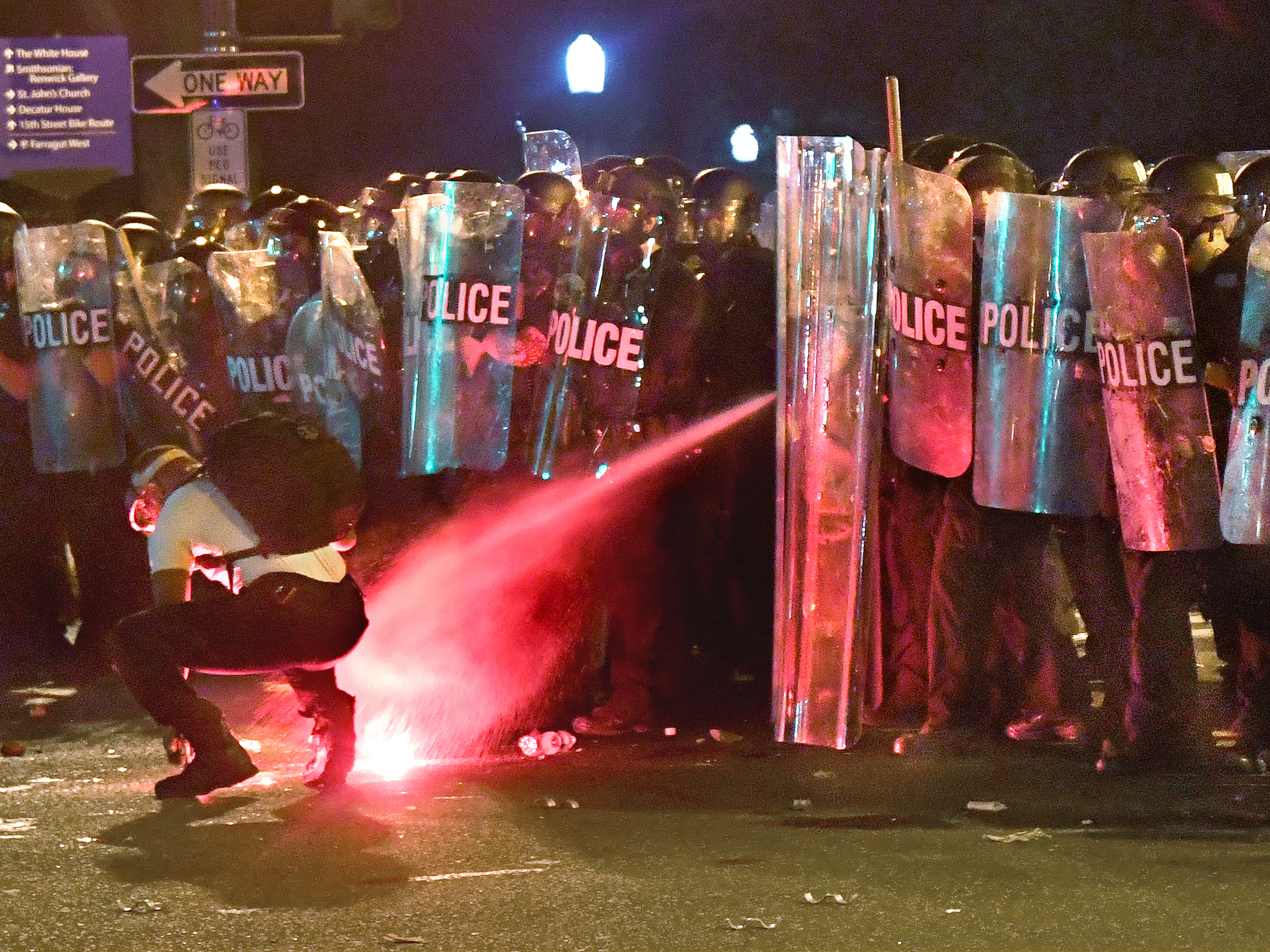 caption: An anti-racism protester near Lafayette Square in Washington, D.C., in May is tear-gassed as he attempts to retrieve a flare thrown at police.