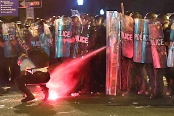 caption: An anti-racism protester near Lafayette Square in Washington, D.C., in May is tear-gassed as he attempts to retrieve a flare thrown at police.