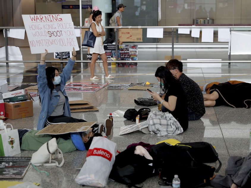 caption: A protester shows a placard to travelers at Hong Kong International Airport on Wednesday. Flight operations resumed at the airport Wednesday morning after two days of disruptions.