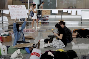 caption: A protester shows a placard to travelers at Hong Kong International Airport on Wednesday. Flight operations resumed at the airport Wednesday morning after two days of disruptions.