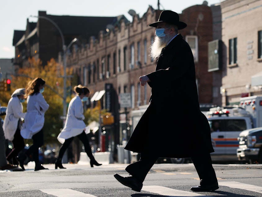 caption: A Hasidic man and medical workers cross paths near the Maimonides Medical Center in Brooklyn, N.Y., in November. When public health messaging comes from community leaders, it's much more likely to be adopted, research on diverse groups finds.