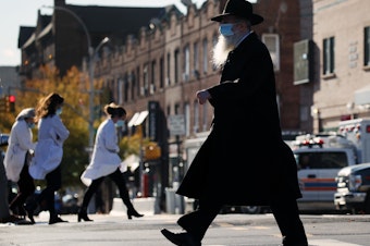 caption: A Hasidic man and medical workers cross paths near the Maimonides Medical Center in Brooklyn, N.Y., in November. When public health messaging comes from community leaders, it's much more likely to be adopted, research on diverse groups finds.