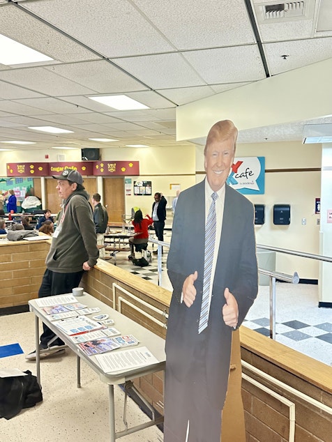 caption: A cardboard Donald Trump gives a double thumbs-up next to a table display of MAGA flyers at Kamiakin Middle School in Kirkland. 