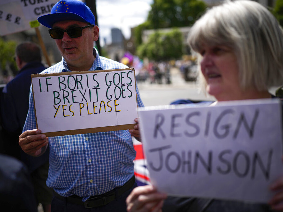 caption: People holds signs as they protest Wednesday outside the Houses of Parliament in London.