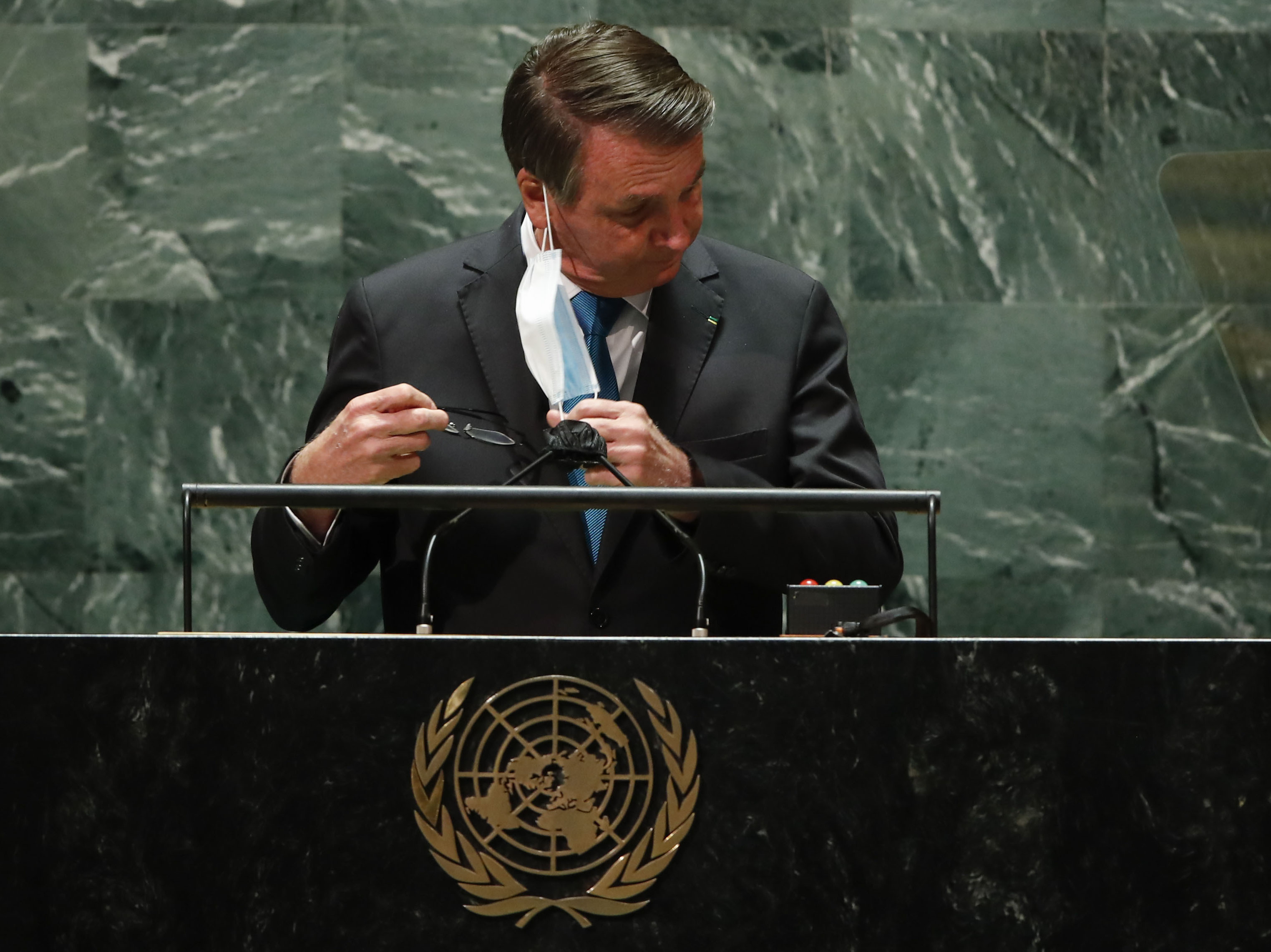 caption: Brazil's President Jair Bolsonaro pulls off his protective face mask to address the 76th Session of the U.N. General Assembly at United Nations headquarters in New York, Tuesday, Sept. 21, 2021.