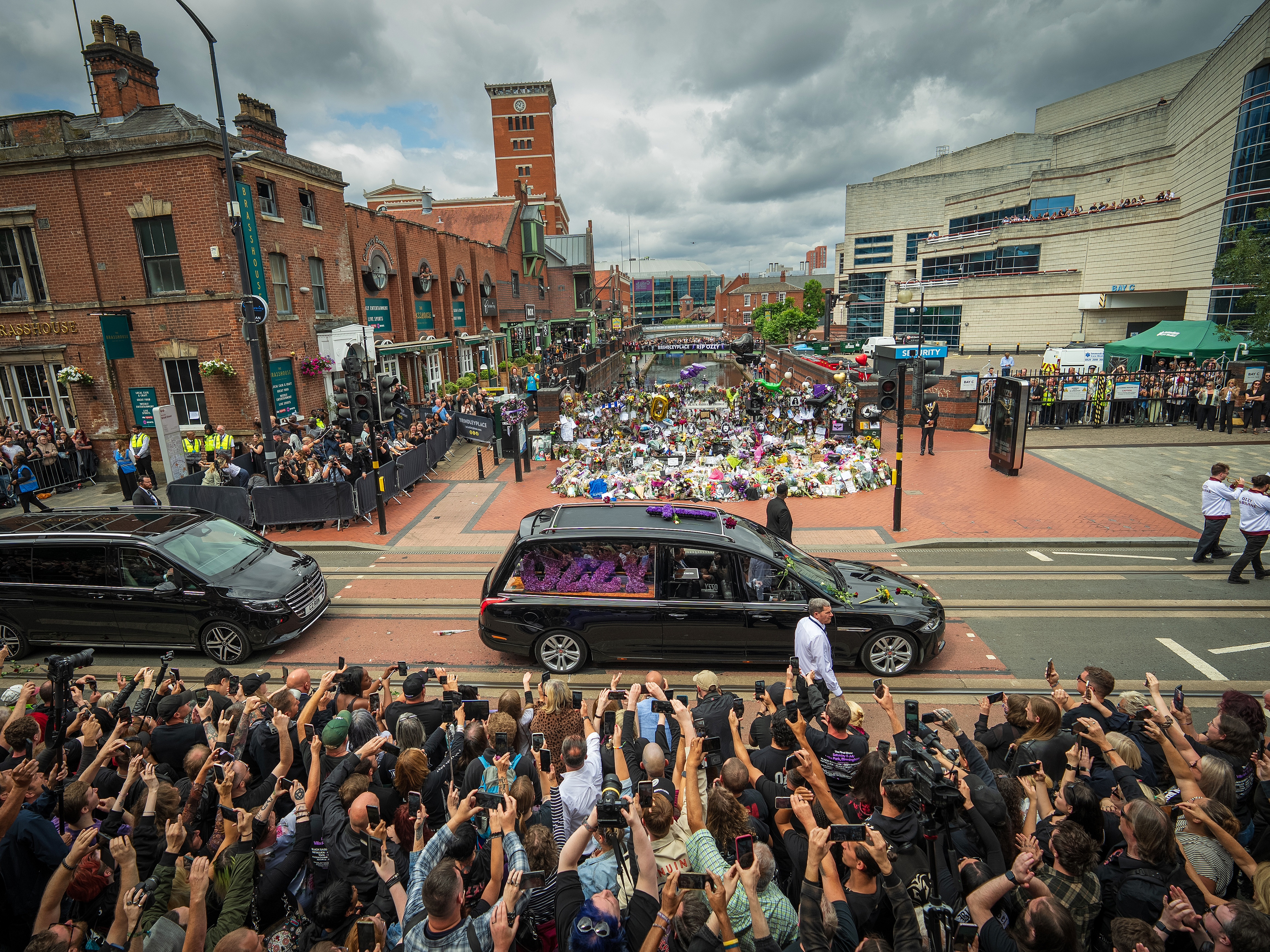 caption: Ozzy Osbourne's funeral cortege makes it way through the streets of Birmingham, England, past the Black Sabbath Bench on Wednesday. The Black Sabbath frontman passed away on July 22, at age of 76.