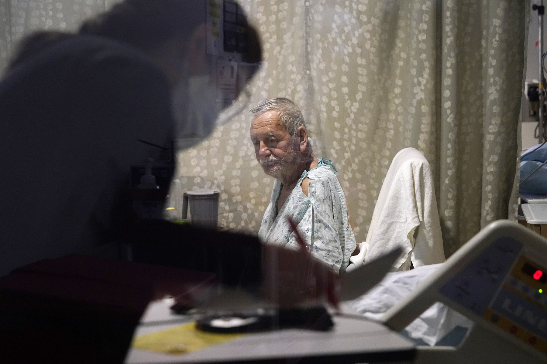 caption: Jesus Aguirre Medina, a Covid-19 patient, looks on as a nutritionist looks over paperwork in his room in the acute care unit of Harborview Medical Center, Friday, Jan. 14, 2022, in Seattle.