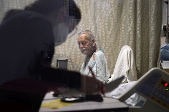 caption: Jesus Aguirre Medina, a Covid-19 patient, looks on as a nutritionist looks over paperwork in his room in the acute care unit of Harborview Medical Center, Friday, Jan. 14, 2022, in Seattle.