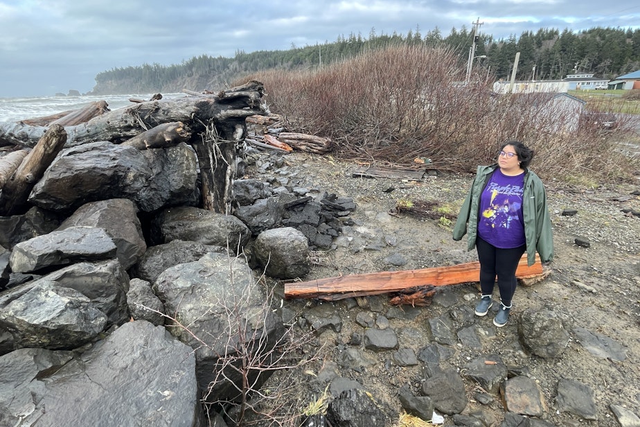caption: Lia Frenchman looks at the driftwood-covered seawall behind her home in Taholah, Washington, on Jan. 11, 2024.