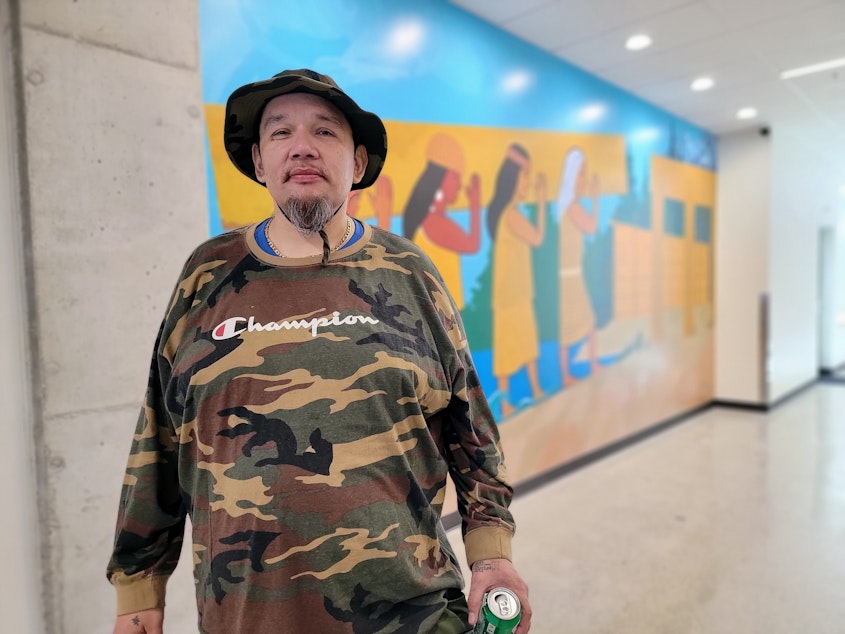 caption: Lorne Briden stands next to a mural at the opening ceremony of Sacred Medicine House on Friday, April 12, 2024.