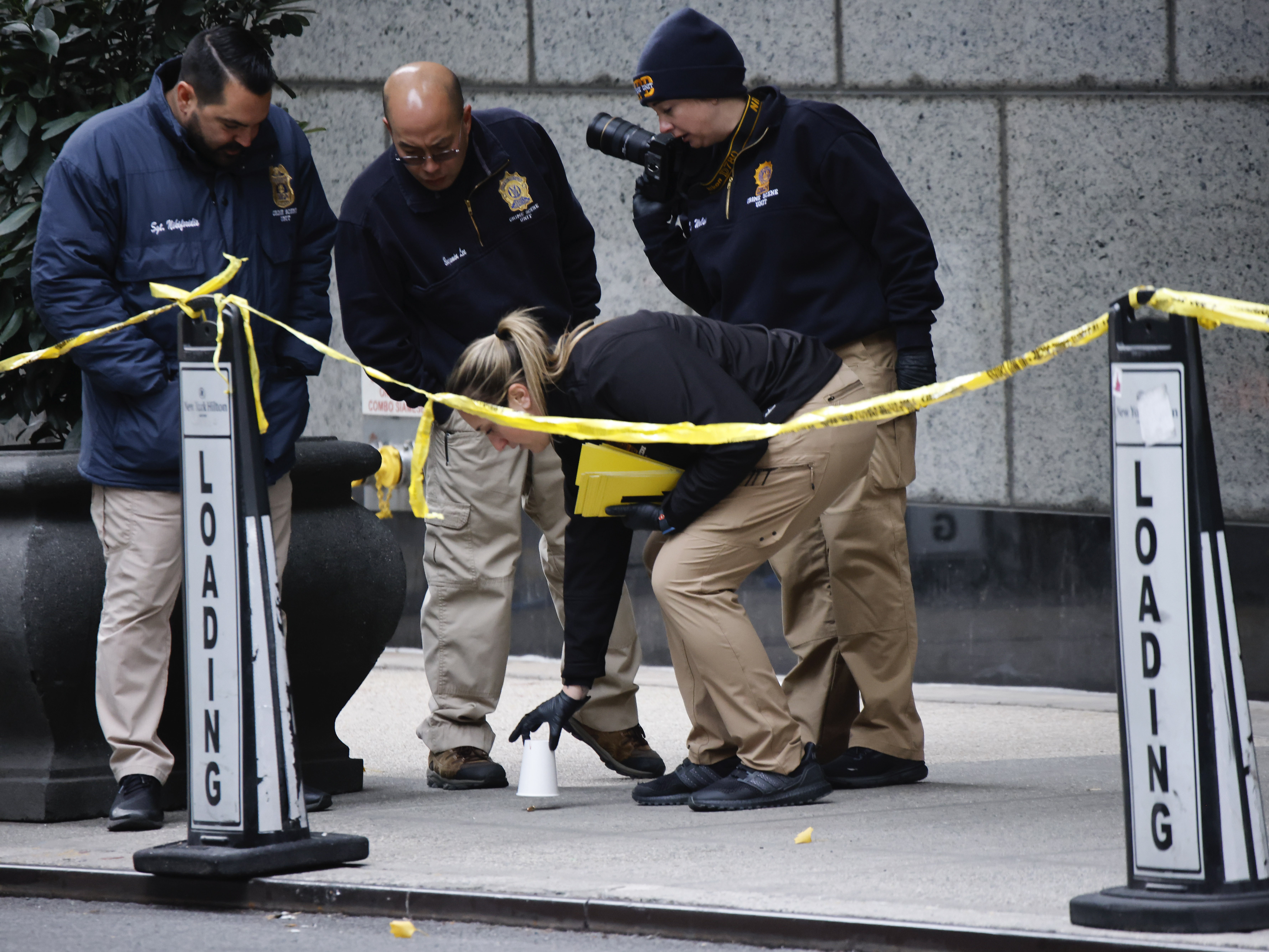 caption: Members of the New York police crime scene unit pick up cups marking the spots where bullets lie as they investigate the scene outside the Hilton Hotel in midtown Manhattan where UnitedHealthcare CEO Brian Thompson was fatally shot on Dec. 4.