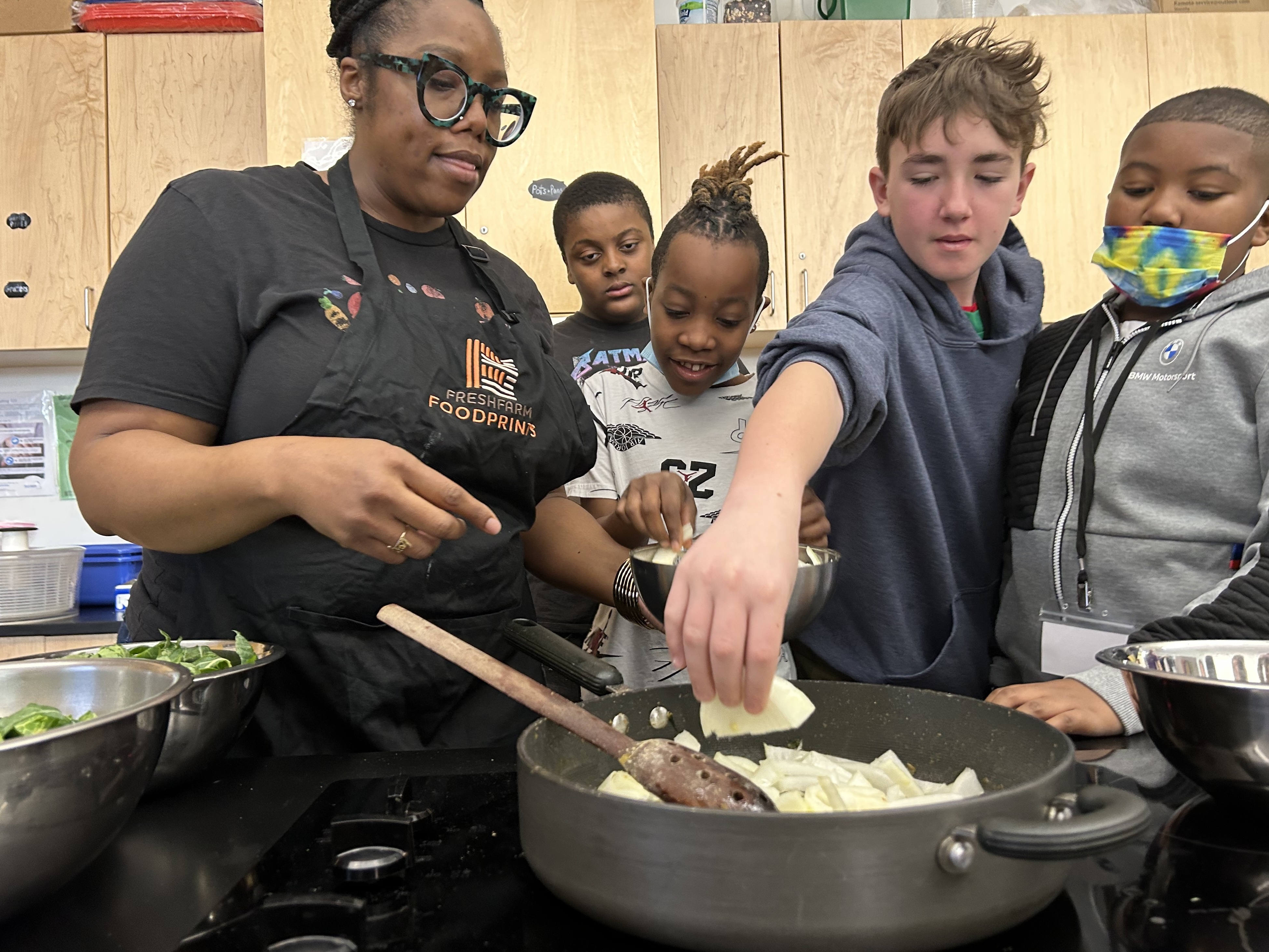 caption: Students help instructional coach Regina Green caramelize onions for a dish featuring fresh greens from the school garden at Watkins Elementary.
