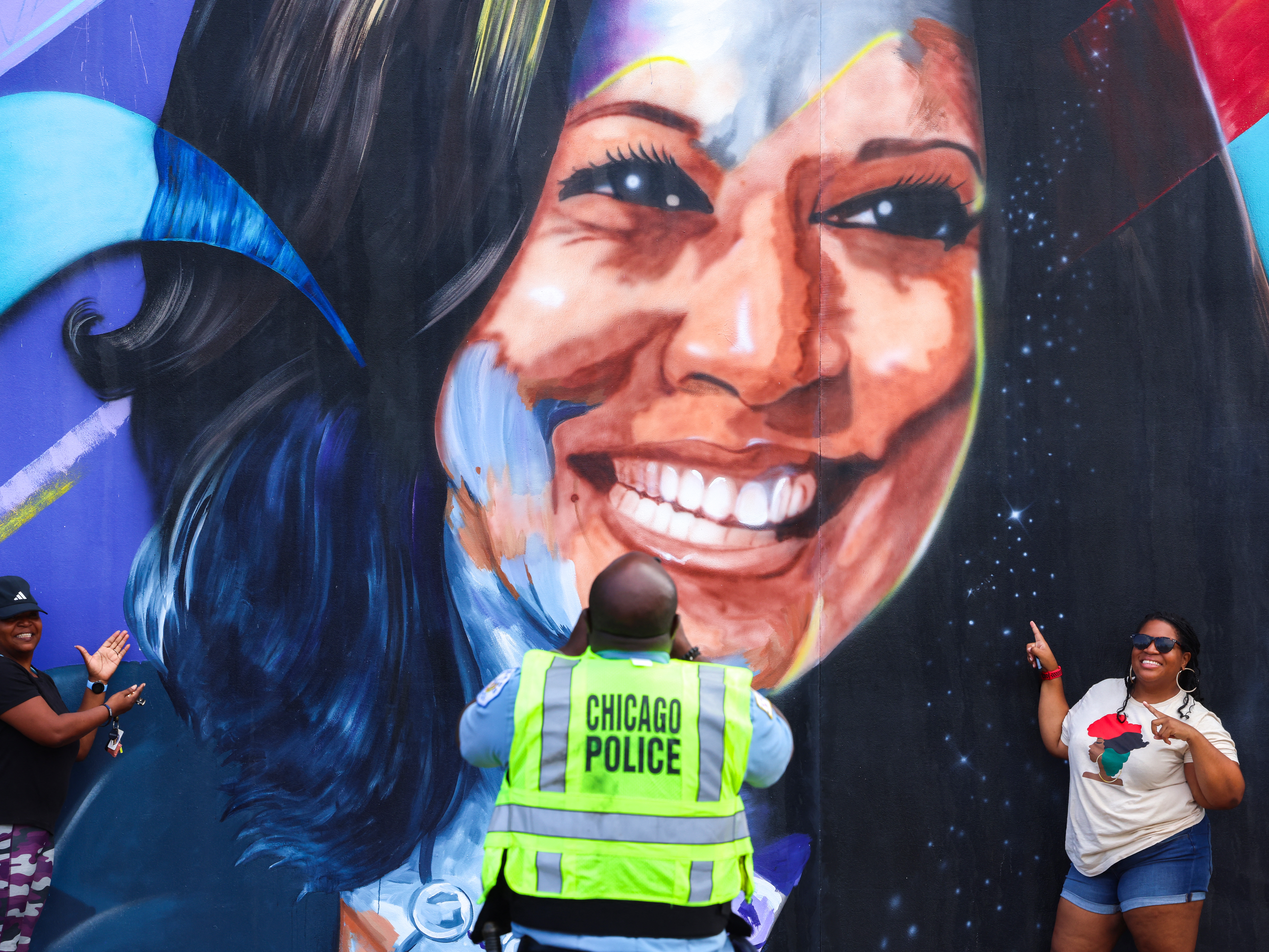caption: A Chicago police officer takes a picture of people posing before a mural of Vice President Kamala Harris outside the Democratic National Convention.