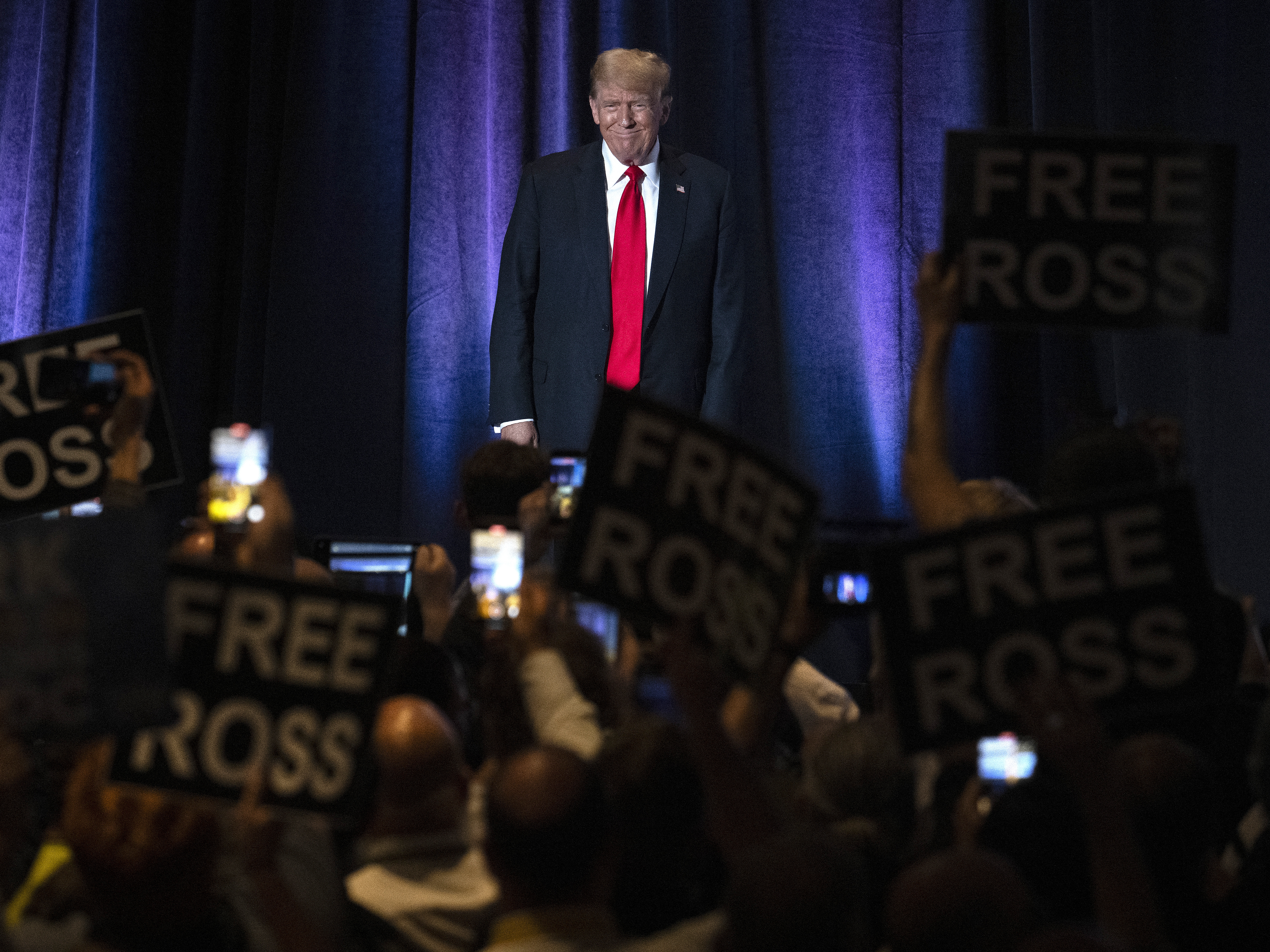caption: People hold up signs reading "Free Ross" as Donald Trump arrives to address the Libertarian National Convention in Washington, D.C, on May 25, 2024. Ross Ulbricht, the founder of the online marketplace Silk Road, was sentenced to life in prison in 2015.
