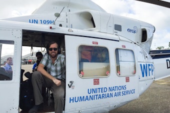 caption: Dr. Eugene Richardson in a helicopter during the Ebola outbreak in Sierra Leone, where he worked as a clinical lead for Partner in Health's response to the outbreak. He is the author of the new book <em>Epidemic Illusions: On the Coloniality of Global Public Health.</em>