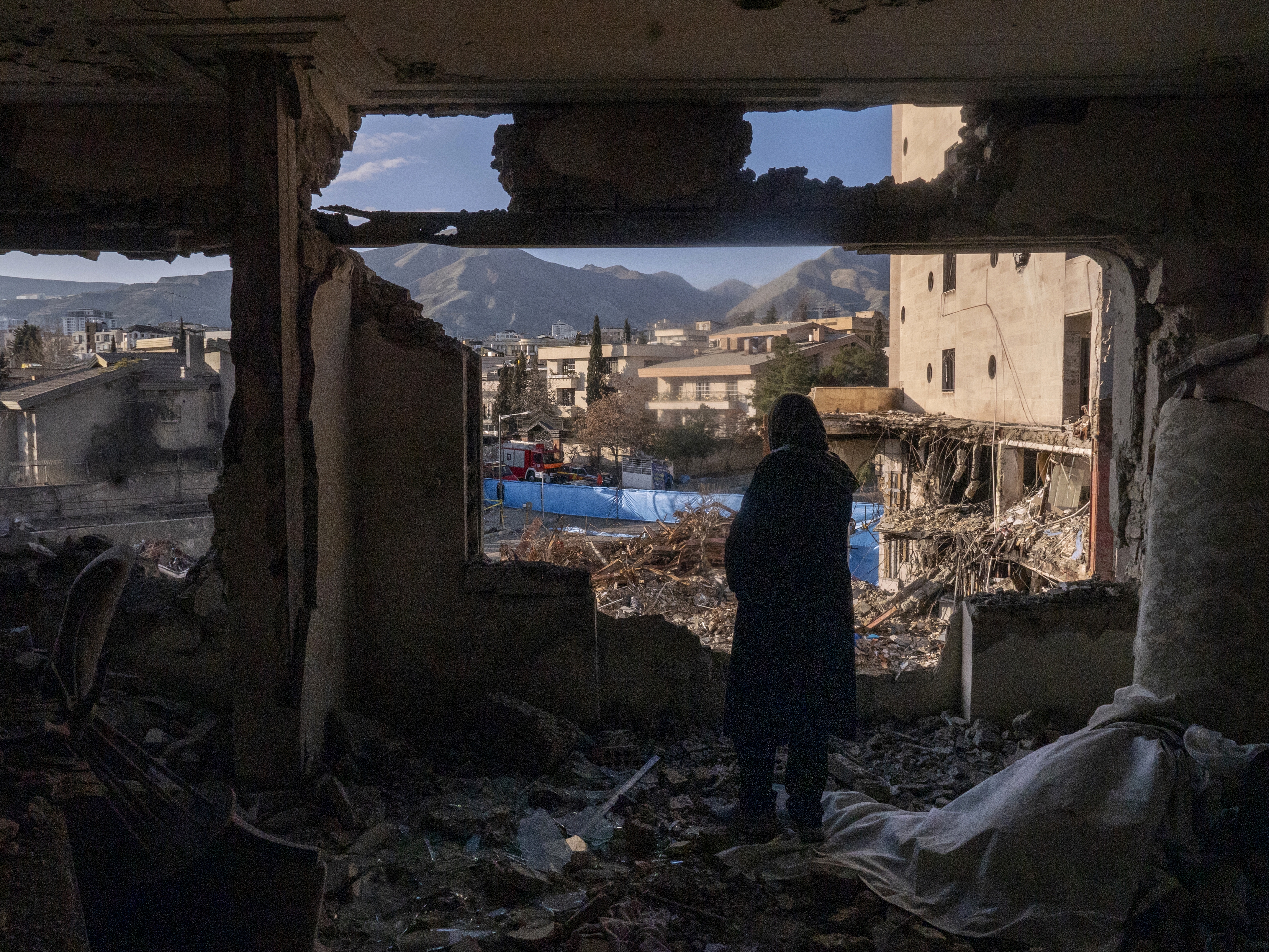 caption: A woman named looks out from her destroyed apartment in the remains of a residential and commercial building in the Shahrak-e Gharb neighborhood of Tehran, Iran, on March 21. The building was hit on March 16 amid U.S. and Israeli attacks and resulted in several deaths.