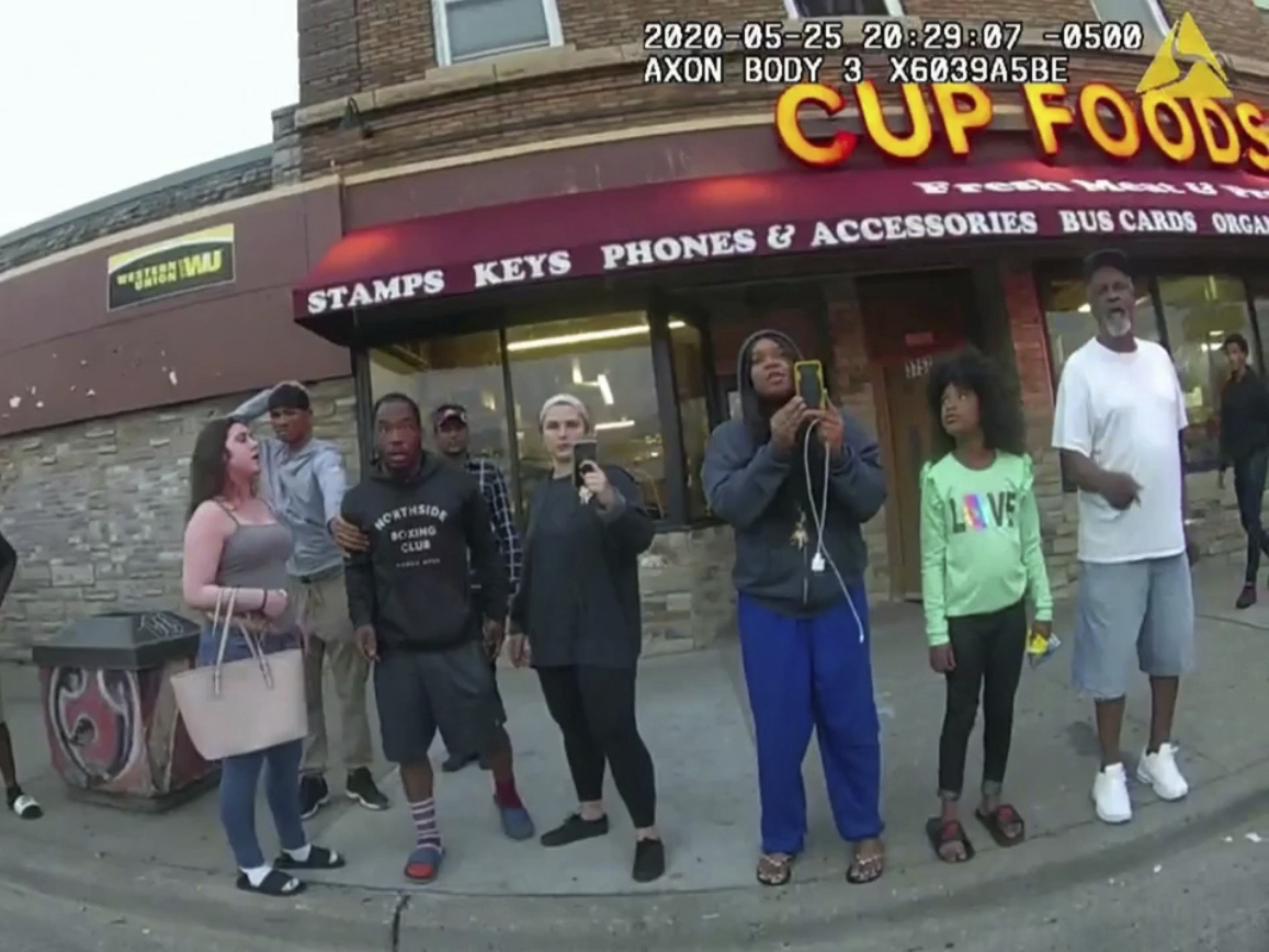 caption: This image from a police body camera shows bystanders including Darnella Frazier (third from right) as Derek Chauvin, who was a police officer at the time, pressed his knee on George Floyd's neck in Minneapolis.