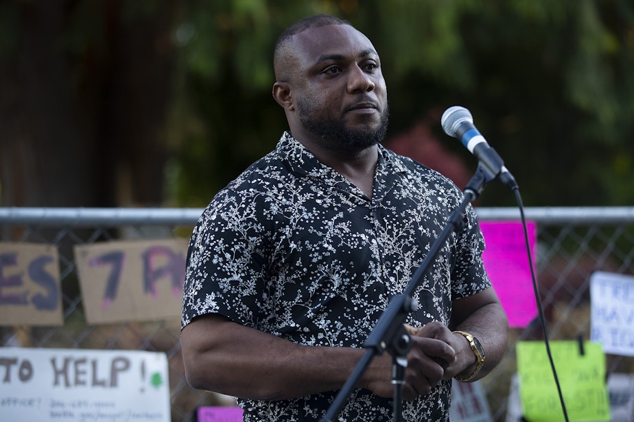 caption: Alex Ayegba of Alex’s Tree Service LLC, the company that was scheduled to cut Luma down, tells the crowd that he will no longer being doing the job, on Tuesday, July 18, 2023, during a gratitude gathering for the roughly 200-year-old culturally modified elder cedar tree in the Wedgwood neighborhood of Seattle. Ayegba also asked for the negative reviews of his business to stop. 