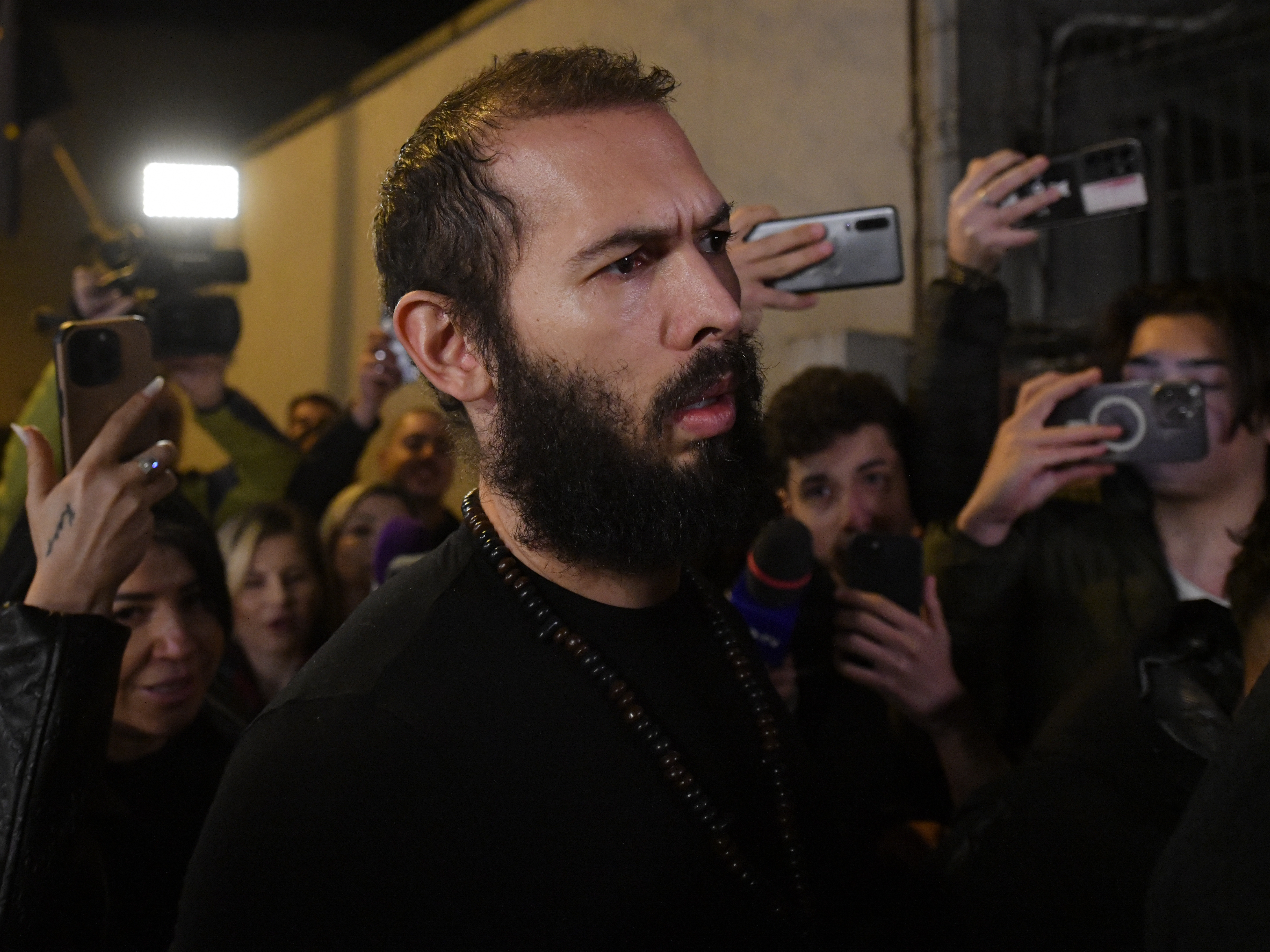 caption: Young fans and media surround Andrew Tate as he leaves a police detention facility in Bucharest, Romania, after his release from prison on Friday.