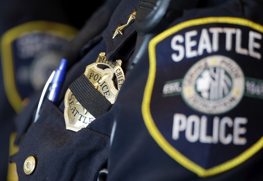 caption: FILE: A black band is drawn across the badge of Seattle Police Deputy Chief Carmen Best as she stands nearby during a news conference on Friday, July 8, 2016, in Seattle. 