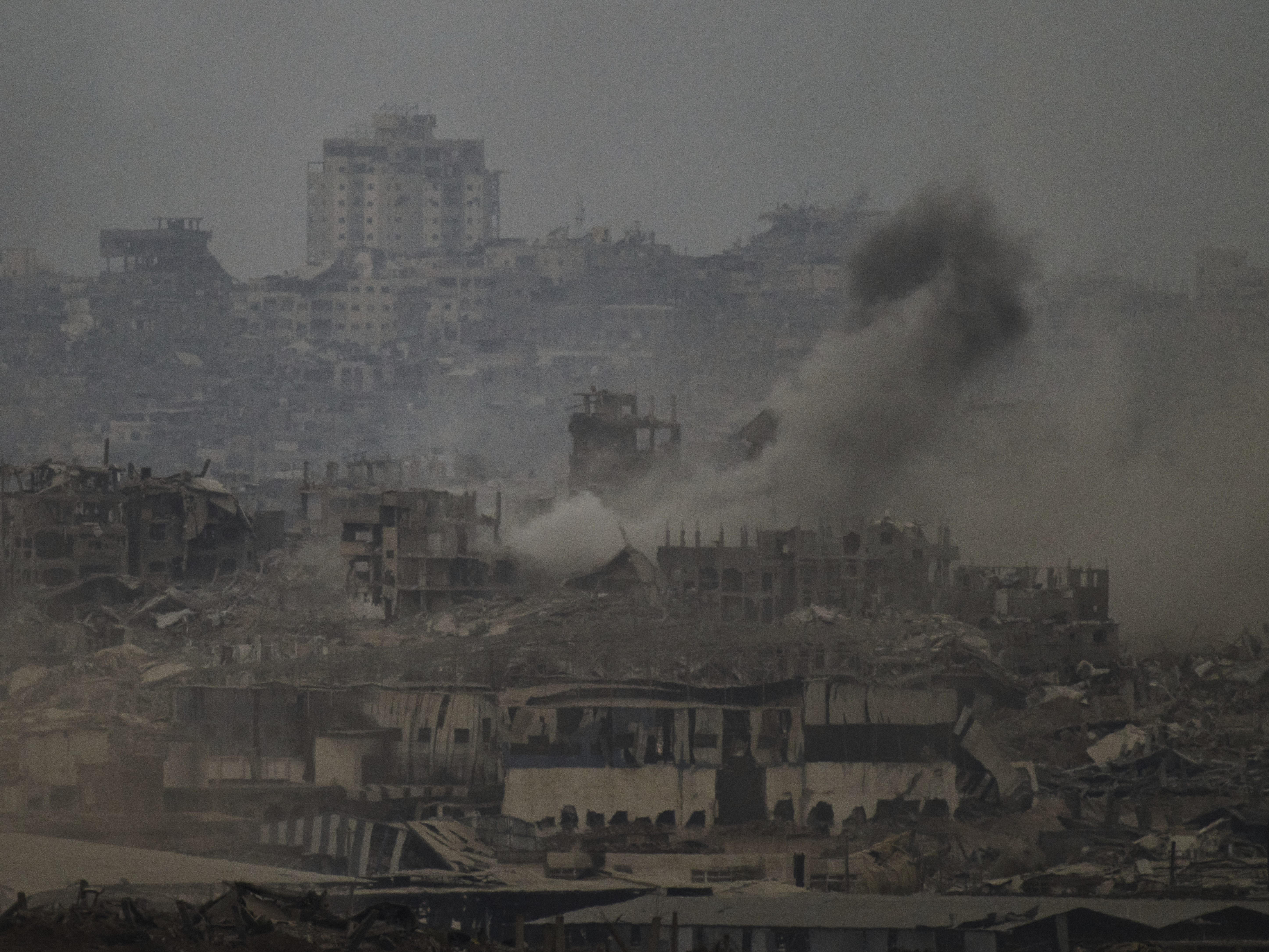 caption: Smoke rises amid destroyed buildings following an Israeli shelling in the Gaza Strip, as seen from southern Israel, Friday, Aug. 1, 2025.