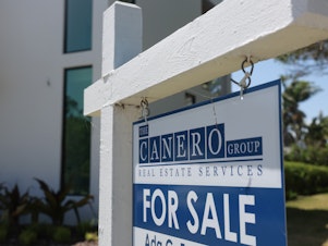 caption: A 'For Sale' sign is posted on the lawn in front of a home on March 15, 2024, in Miami, Fla. The National Association of Realtors announced that it had reached a nationwide $418 settlement of claims that the industry had conspired to keep agent commissions high.
